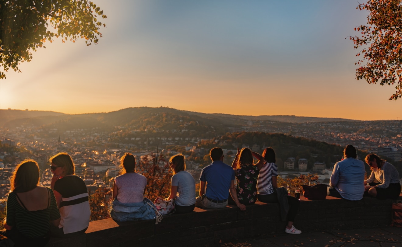 Junge Menschen sitzen auf Mauer hoch über Stuttgart und blicken auf den Sonnenuntergang
