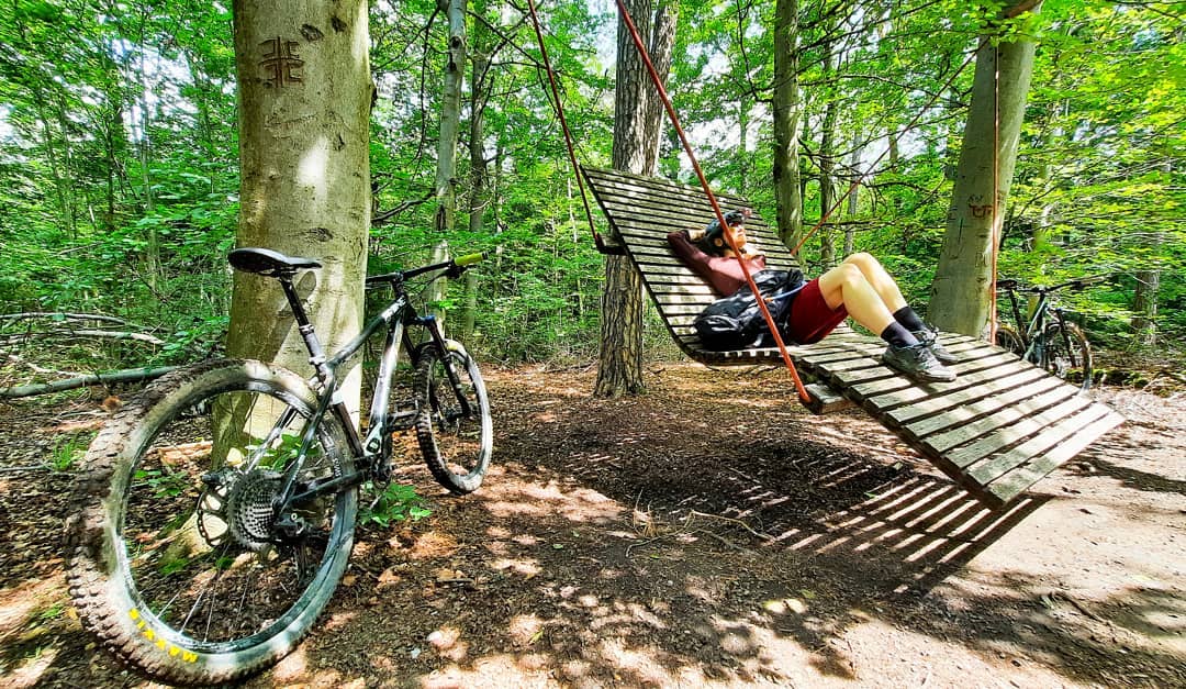 Mountainbiker liegt auf Waldsofa, Fahrrad an Baum gelehnt daneben